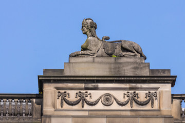 Obraz premium Edinburgh, Scotland, UK - June 13, 2012; Sphinx statue at edge of roof of Parliament House, where Supreme Courts of Scotland reside. Blackened brown stone against blue sky.