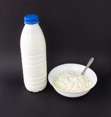 A bottle of milk and a plate of cottage cheese on a black background, close-up, genetic