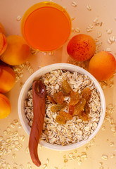 Healthy breakfast. White plate of oatmeal with dried apricots, a glass of an apricot juice and fresh apricots on a white table.