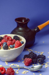 Healthy breakfast. White plate with oatmeal strewn and different berries on a blue background. Summer harvest.