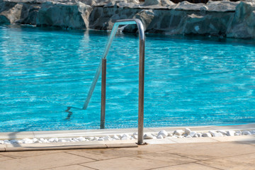 Metal handrail of an empty outdoor pool with decoration of small white rocks.