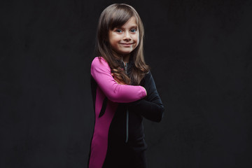 Fototapeta premium Smiling little girl dressed in sportswear standing with crossed arms. Isolated on dark textured background.