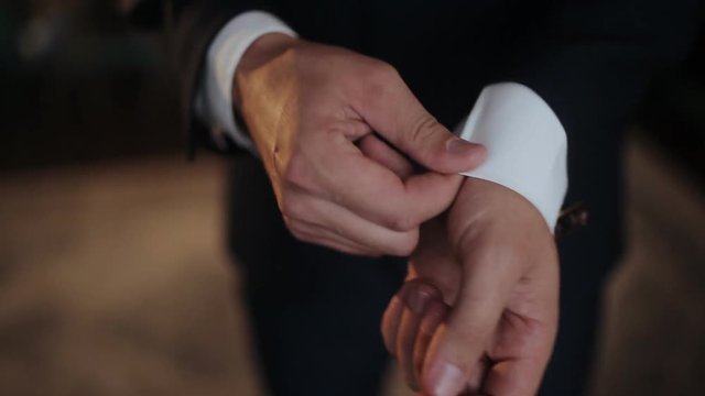 A young man in black suit adjusts his cufflinks of white shirt.