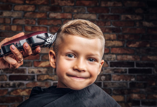 Close-up portrait of a cute smiling boy getting haircut against a brick wall.