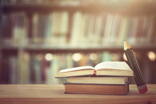 back to school concept. stack of books over wooden desk in front of library and shelves with books.