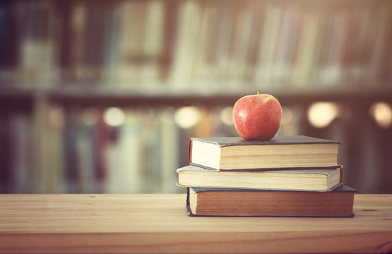 back to school concept. stack of books over wooden desk in front of library and shelves with books.