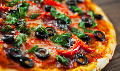 Pizza with Mozzarella cheese, salami, pepper, pepperoni, Tomatoes, olives, Spices and Fresh Basil. Italian pizza on wooden background