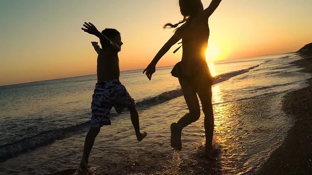 Happy children playing on the beach at the sunset time. Two Kids having fun outdoors. Concept of summer vacation and friendly family.