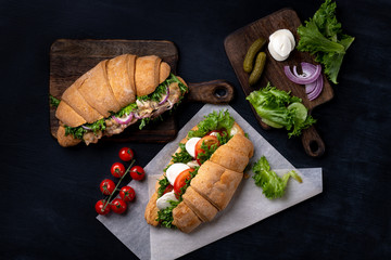 Croissant sandwiches with fresh vegetables and fried meat on the wooden board on black background, top view