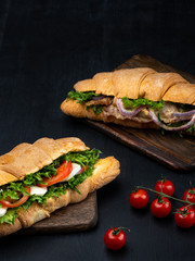 Croissant sandwiches with fresh vegetables, ham  and cheese on black wooden background. vertical