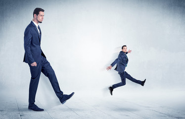 Big businessman kicking small businessman who is flying away with his briefcase on his hand
