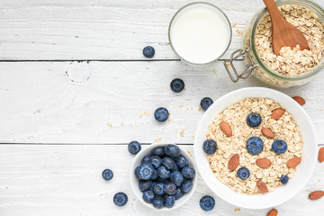 Oat flakes with fresh blueberries, milk and nuts on a white wooden table. healthy breakfast. top view