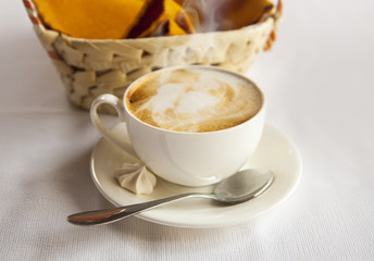 White cup with coffee. Cappuccino. Basket and coffee with a small cake and a spoon. Background blur.