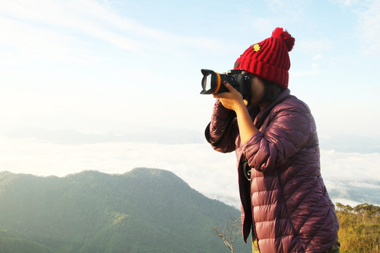 a young hiker girl taking a pictures with her camera above the clouds on the mountain peak.