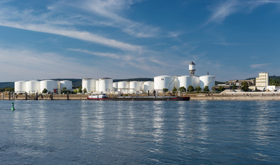 Storage silos,fuel depot of petroleum and gasoline on the banks of the river in western Germany on a beautiful blue sky with clouds. Visible tanker barge.