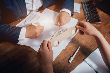 Man signing a car insurance policy, the agent is holding the wooden car model.