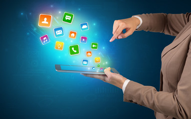 Hand holding tablet and application icons falling inwards
