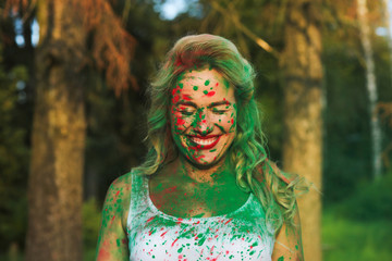Laughing caucasian blonde woman with bright makeup posing covered by Holi paint