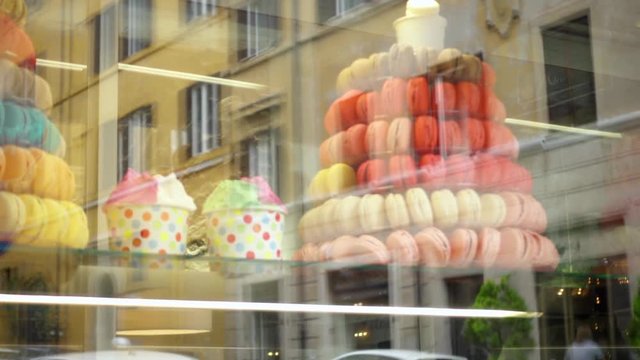 Colorful fresh macarons behind glass showcase. Street and house reflections in storefront with sweet french cookies. Beautiful bakery shop-window decoration