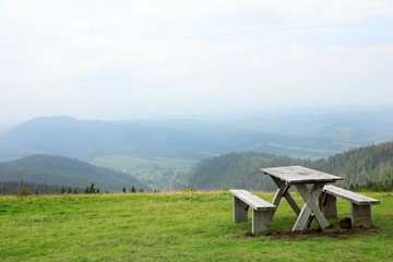 Picturesque landscape with wooden picnic table and mountain forest on background