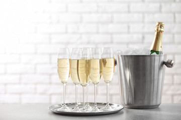 Glasses with champagne and bottle in bucket on table against brick wall
