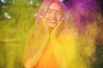Laughing young model posing with exploding yellow paint at summer Holi festival