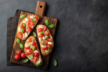 Bruschetta with tomatoes, mozzarella cheese and basil on a cutting board. Traditional italian appetizer or snack, antipasto. Top view with copy space. Flat lay