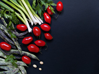 Tomatoes, parsley, green onions, green beans lie on a dark background