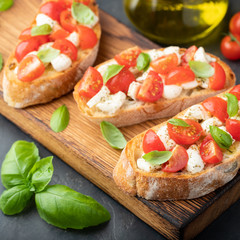 Bruschetta with tomatoes, mozzarella cheese and basil on a cutting board. Traditional italian appetizer or snack, antipasto