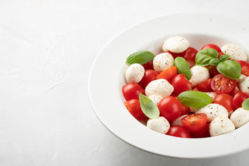 White plate of classic delicious caprese salad with ripe tomatoes, mozzarella and fresh basil leaves on gray background with copy space. Italian food. The concept of a healthy vegetarian diet