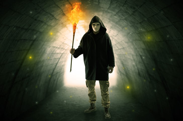 Ugly man with burning flambeau walking in a dark tunnel