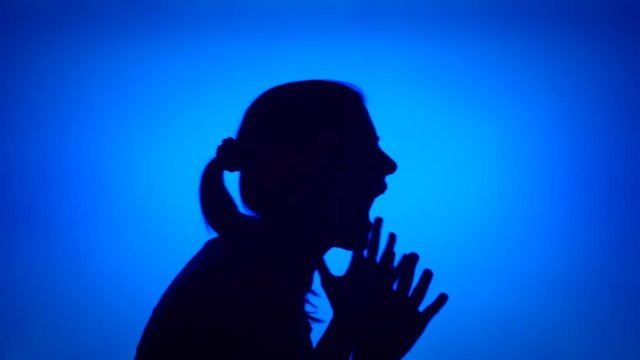 Silhouette of young frustrated woman crying. Female's face in profile screaming in despair on blue background. Black contour shadow of teenager's half-face showing strong negative emotions