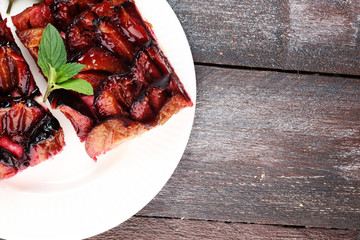 Rustic plum cake on wooden background with plums around.