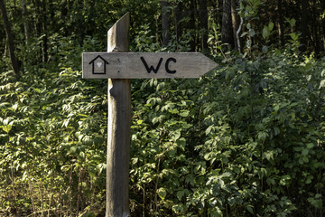 wooden post in the forest, with a sign and an inscription wc