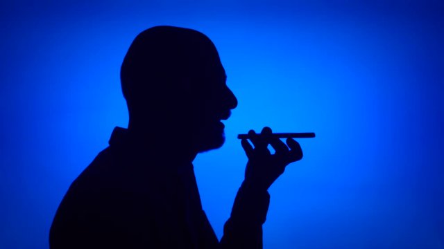 Silhouette of senior man using mobile on blue background. Male's face in profile talking on cellphone. Black contur shadow of grandfather's half-face