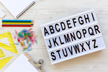 Back to school concept. Letters from A to Z. English alphabet on modern board and accessories for study over white wooden surface, overhead view. From above, flat lay.