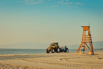 Tractor cleaning the beach on a calm morning at the beach with a safeguard post on a sunny morning...