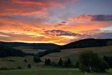 Sauerland, Germany - Dramatic pink and orange sunset over a green valley with wooded hills in the distance