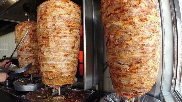 Chef Cutting Grilled Meat Off Rotating Skewer / A gyro or gyros is a Greek dish made of meat cooked on a vertical rotisserie, traditionally pork, or chicken