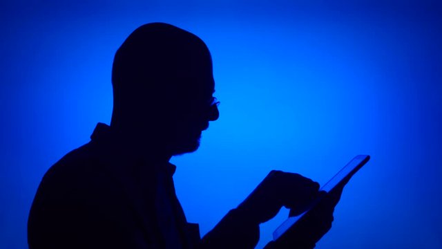 Silhouette of senior man use tablet on blue background. Male's face in profile browse, read, chat online with family and friends on computer. Black contur shadow of grandfather's half-face