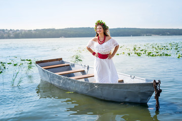 Beautiful girl in national dress in boat on lake