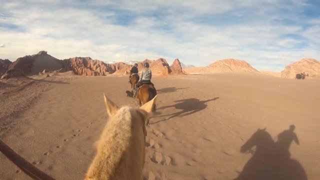 People riding horse slow mo at the San Pedro De Atacama desert Chile. Three person in a line going forward one behind filming