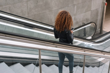frau steht auf der rolltreppe auf dem weg zur u-bahn und schaut auf ihr handy
