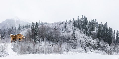 Panoramic view of an snow covered winter forest. Unfinished house on the hill in Dombai ski resort suburb.