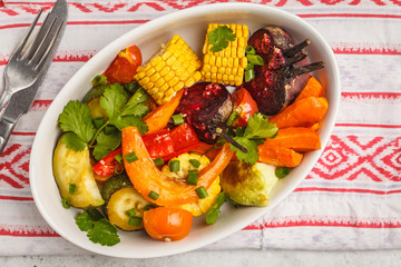 Baked vegetables: pumpkin, beets, carrots, peppers, zucchini and corn in white dish, white background.