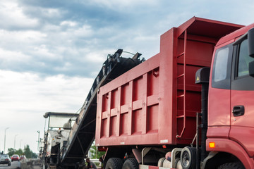 Road construction site. Asphalt milling grinds machine loading used asphalt into dump truck for...