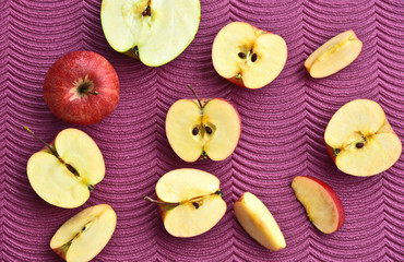 Many sliced red Gala apples on purple background.