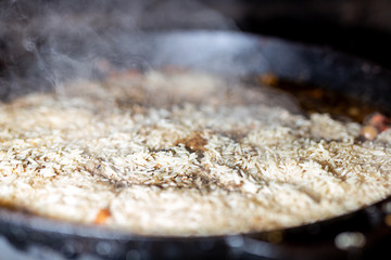 cooking Rice for pilaw or paella in iron cauldron over open fire. Smoke and steam. Tasty food preparing outdoor process background
