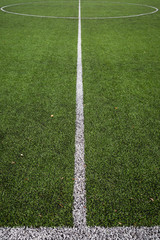 Closeup of green artificial grass soccer field with white line and center circle. © goodmoments