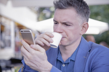 Young successful businessman holding  phone and drinking coffee
